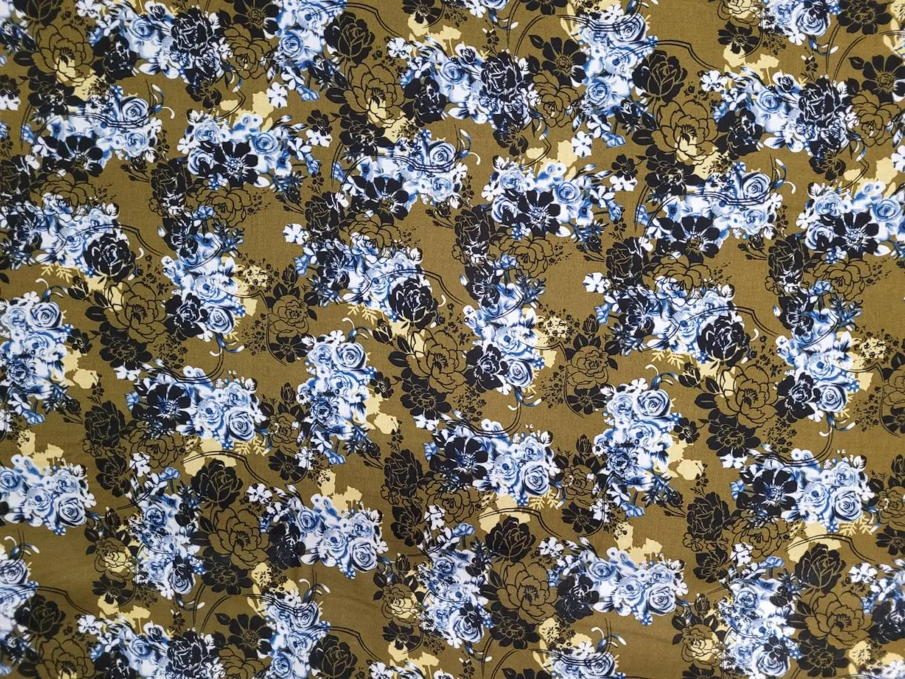 Floral10 Collection in Olive Green. Olive-green ground scattered with sky-blue and white blossoms over darker green leaves.
